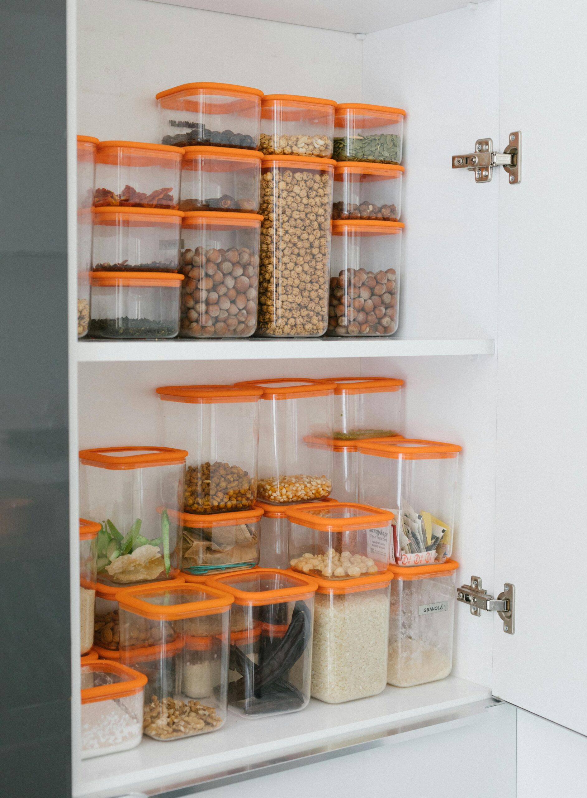 Neatly organized pantry shelves featuring diverse grains and seeds in transparent containers with orange lids.