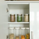 Neatly organized kitchen cabinet with various food items in jars and containers on shelves.